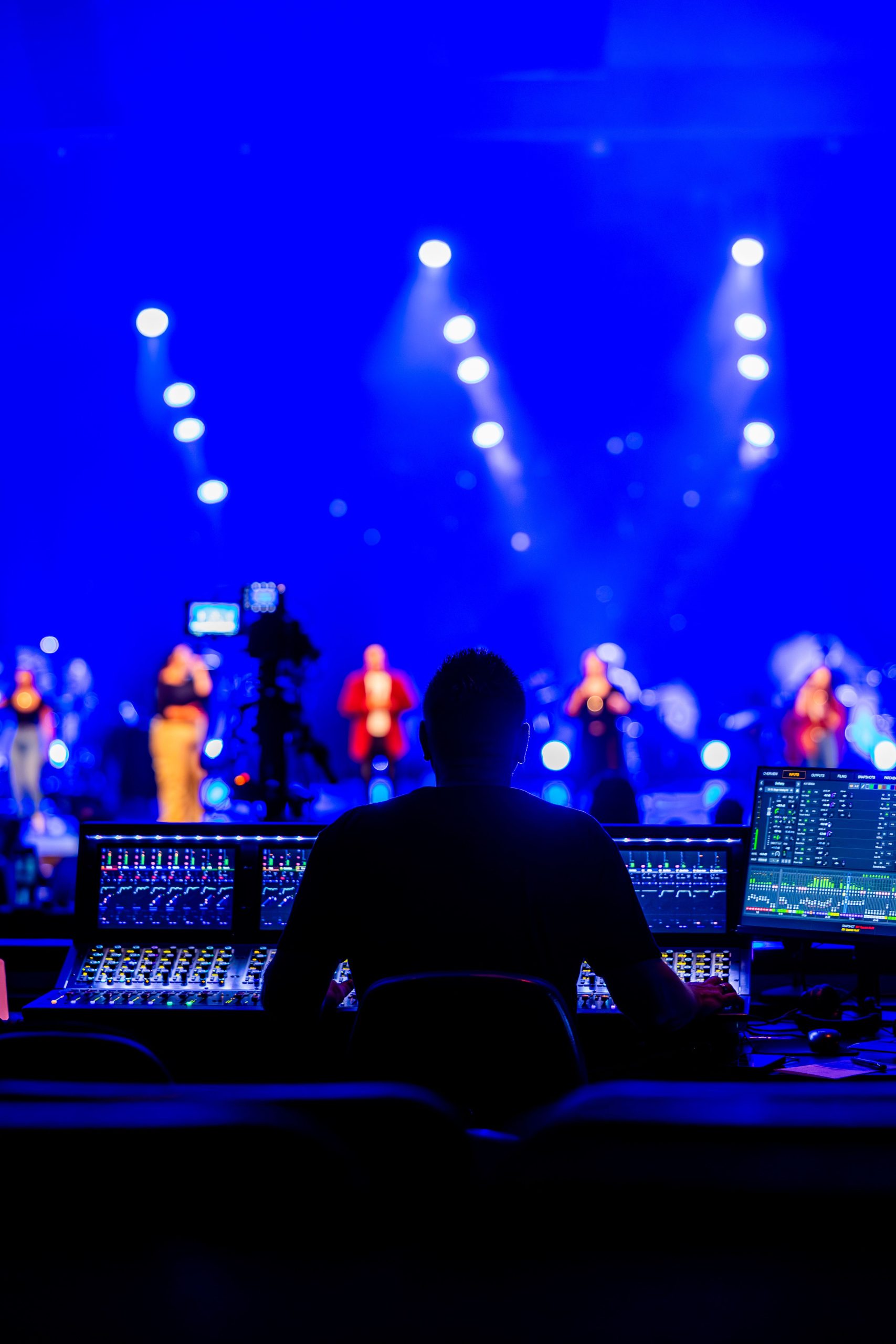 Sound engineer managing live concert with vibrant blue stage lighting.